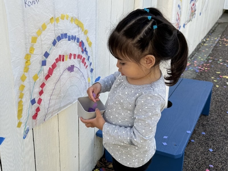 child creating rainbow art outdoors at preschool in hayes valley san francisco